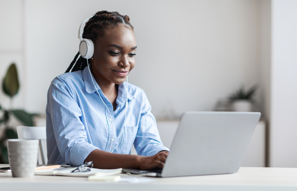 young woman with headphones on typing on her laptop computer